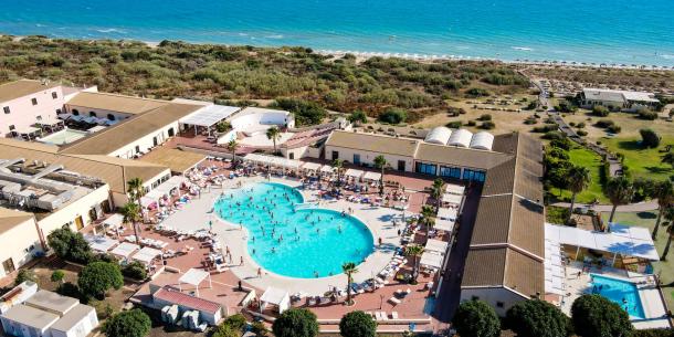 Vista aerea di un resort con piscina, spiaggia e mare blu.
