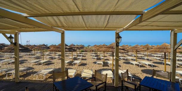 Spiaggia deserta, ombrelloni di paglia e mare blu, atmosfera di pace e relax.