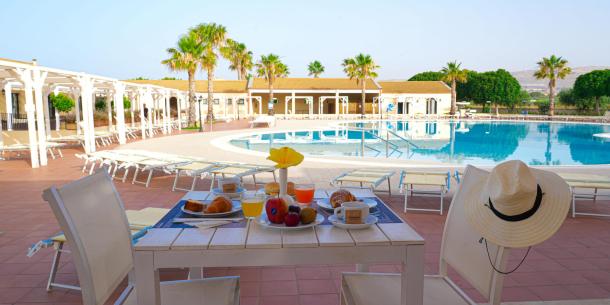Colazione rilassante a bordo piscina, con frutta, croissant e sole splendente.