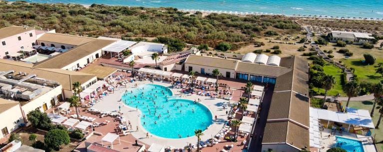 Vista aerea di un resort con piscina, spiaggia e mare blu.