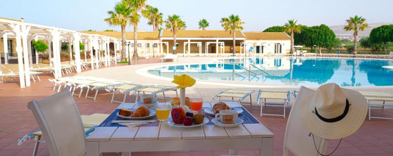 Colazione rilassante a bordo piscina, con frutta, croissant e sole splendente.