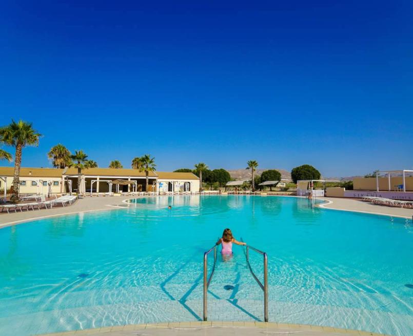 Piscina azzurra, cielo limpido, palme, relax e serenità in un resort soleggiato.
